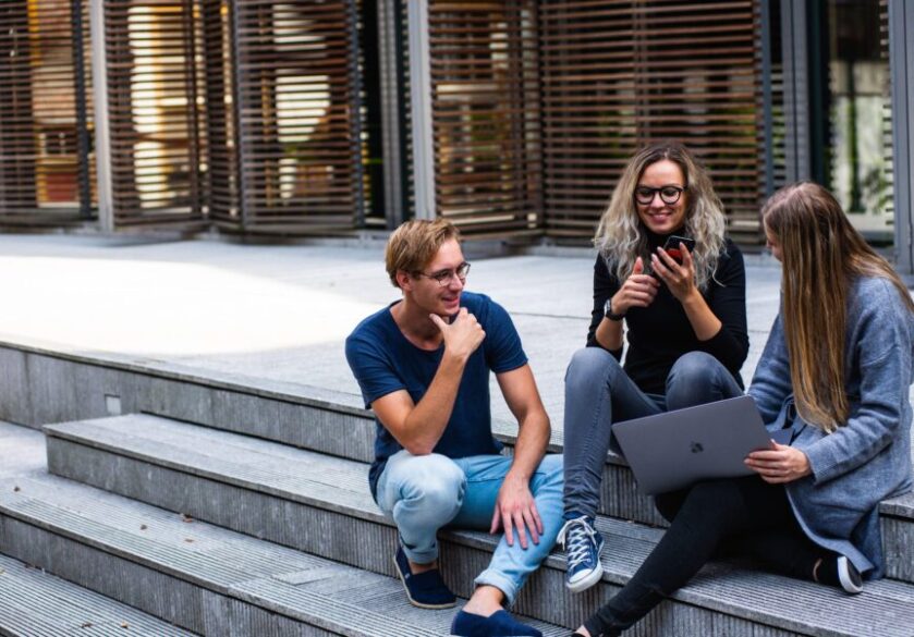 Three creative workers sit on the steps outside with a laptop